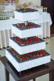 Tort weselny na kwadratowym stelażu wysypany owocami